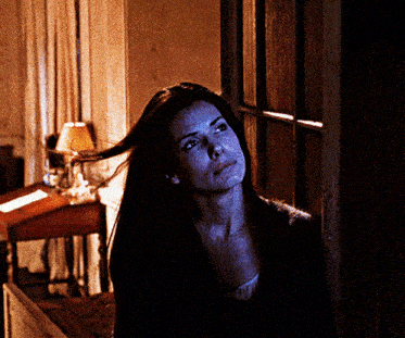 a woman with long hair stands in a dark room looking up