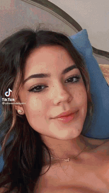 a woman is laying on a bed with a blue pillow and a tiktok icon on her face
