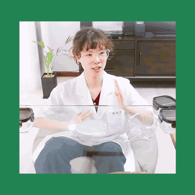 a woman in a lab coat and glasses sits at a table with containers