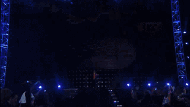 a crowd of people are gathered in front of a stage with a large screen behind them that says ' a ' on it
