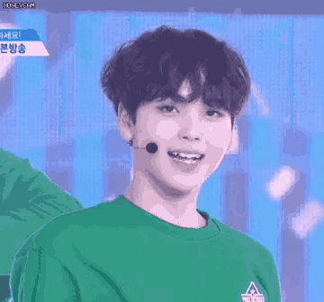 a young man wearing a green shirt and a microphone looks at the camera