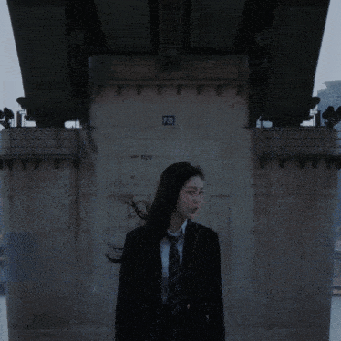 a woman in a suit and tie is standing under a bridge with the number 120 on the side