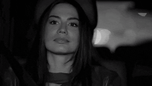 a black and white photo of a woman sitting in the back seat of a car .