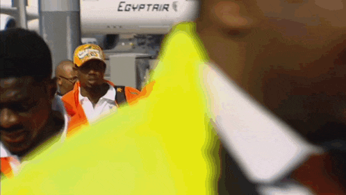 a man wearing a hat that says ' egyptair ' on it walks in front of an airplane