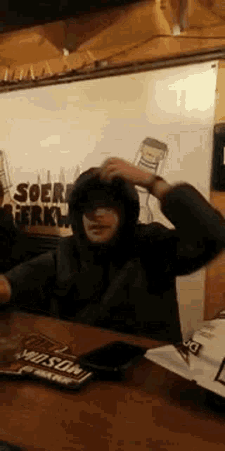 a man in a hoodie is sitting at a table in front of a whiteboard .