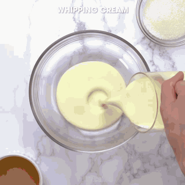 a person pouring whipping cream into a glass bowl