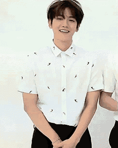 a young man in a white shirt and black pants is standing with his hands folded .
