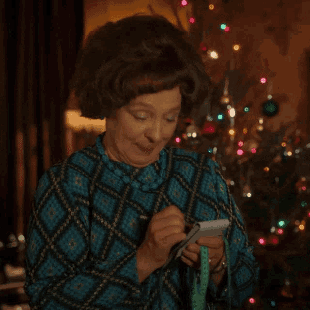 a woman in a blue dress is holding a measuring tape and a cell phone in front of a christmas tree