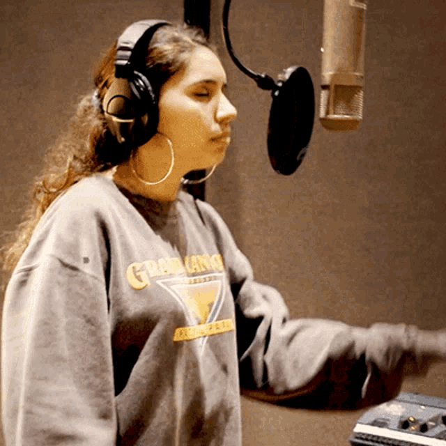 a woman wearing headphones and a gray sweatshirt that says grad king on it