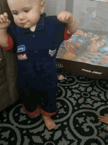 a baby standing in front of a pack n play