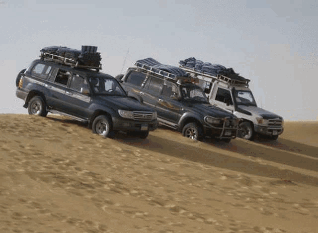 three cars are parked on top of a sand dune .