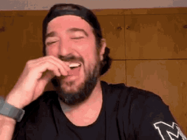 a man with a beard is laughing with his eyes closed while wearing a hat .