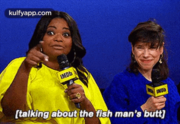 two women are talking into microphones and one of them is pointing at the other .
