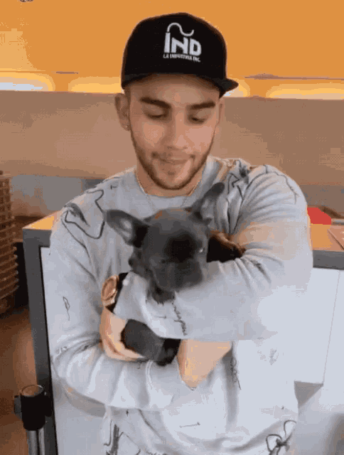 a man wearing a hat that says ind is holding a small black dog