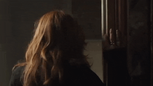 a woman with long red hair is looking out of a window .