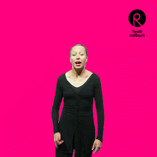 a woman in a black jumpsuit stands in front of a pink background
