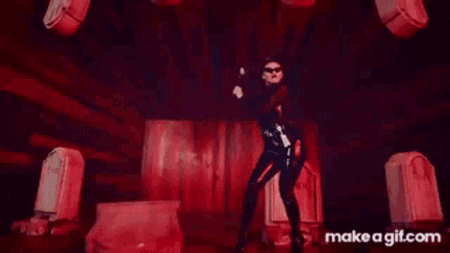 a woman in a black latex suit is dancing in a dark room with a lot of red lights .