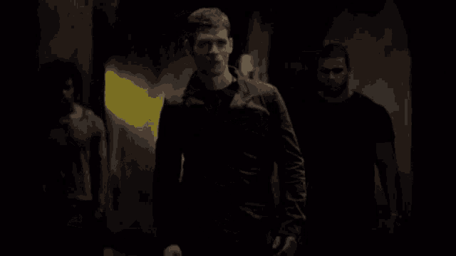a man in a black jacket is walking in a dark room with two other men .