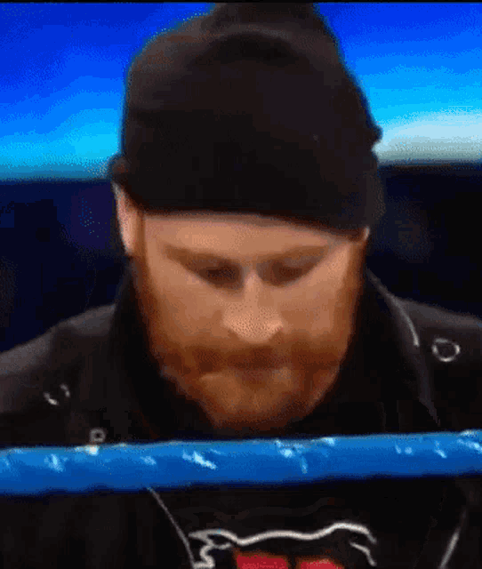a man with a beard is sitting in a boxing ring wearing a black hat .