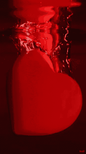 a red heart is floating in a glass of red liquid