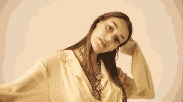 a woman wearing a yellow striped shirt and a gold necklace looks at the camera
