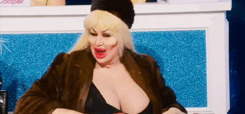 a woman wearing a fur coat and a black bra is sitting in front of a blue wall .