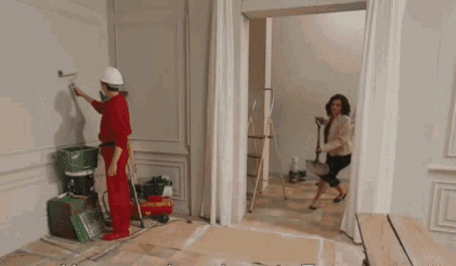 a man is painting a wall while a woman looks on .