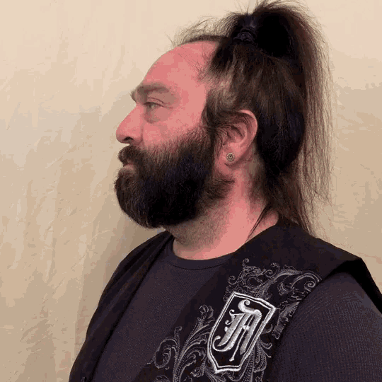 a man with a beard is wearing a black vest with the letter h on it