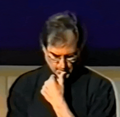 a man wearing glasses and a black shirt holds his hand to his chin
