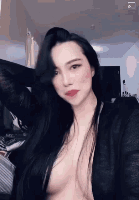 a woman with long black hair is taking a selfie while wearing a very revealing black top .