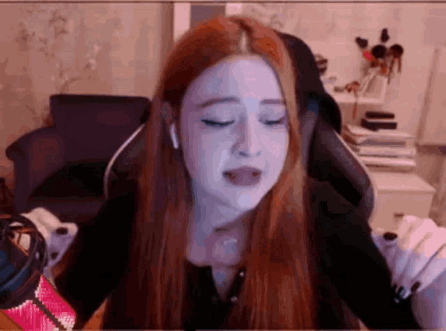 a girl with long red hair is sitting in a chair with her eyes closed .