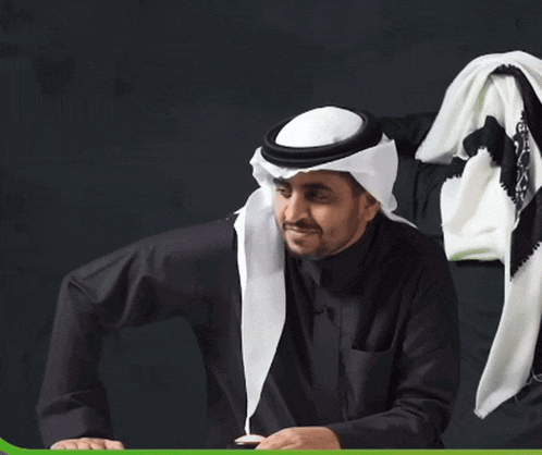 a man wearing a black shirt and a white scarf is sitting at a desk
