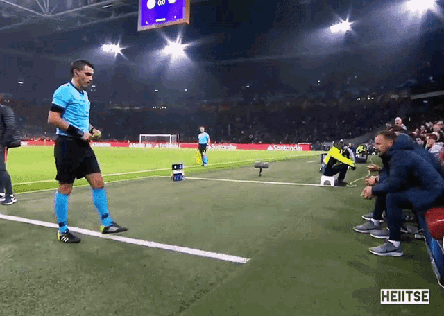 a referee stands on the sidelines of a soccer field in front of a santander banner