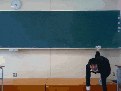 a man is doing a handstand in front of a blackboard with a clock on it
