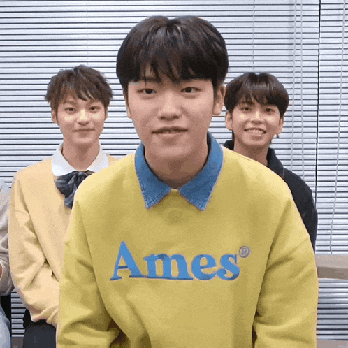 a boy wearing a yellow ames sweatshirt stands in front of a window