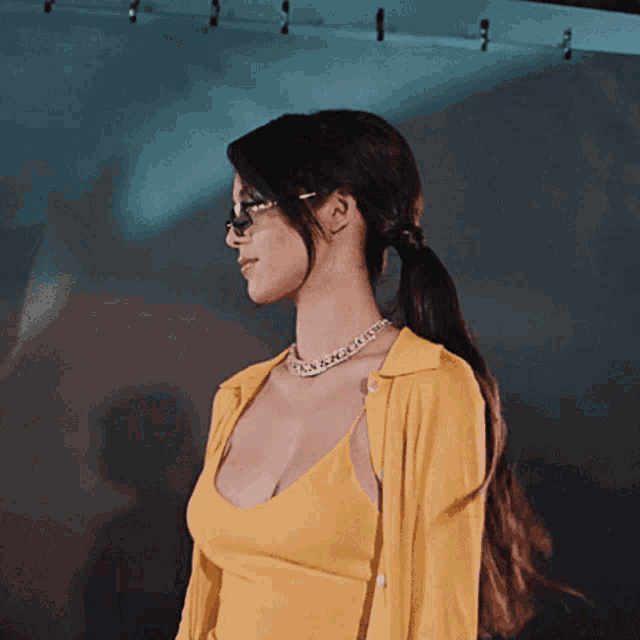 a woman wearing glasses and a yellow top is looking to the side