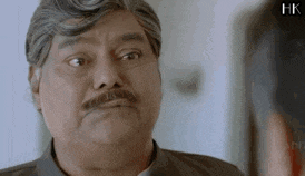 a man with a mustache is making a funny face in front of another man .