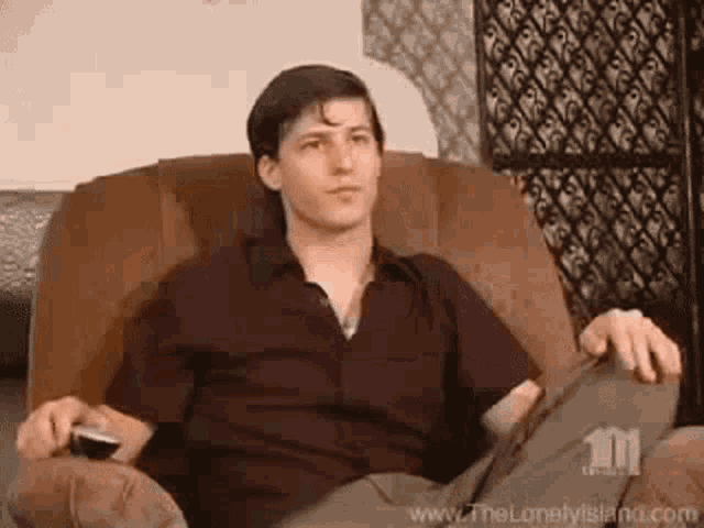 a man is sitting in a chair holding a remote control and watching tv .