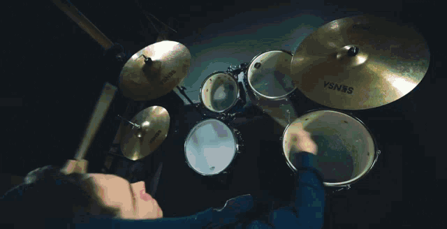 a man playing drums in a dark room with a diamond on the wall behind him