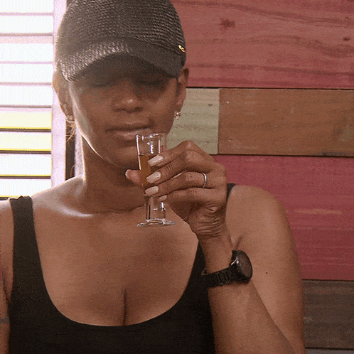 a woman wearing a hat is holding a shot glass in her hand