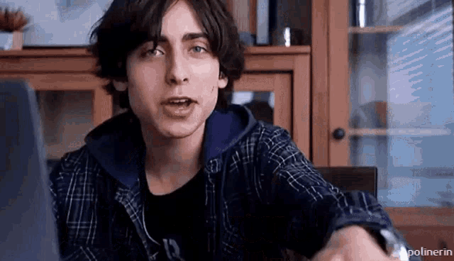 a young man in a plaid shirt is sitting at a table with a laptop .