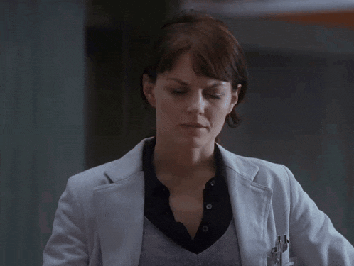 a woman wearing a white coat and a black shirt is giving a peace sign