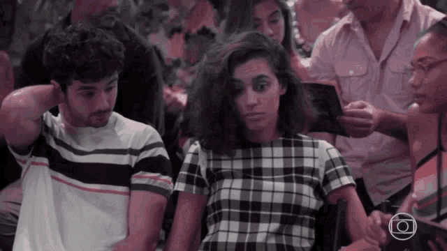 a woman in a plaid shirt sits next to a man in a striped shirt in a crowd