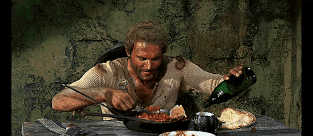a man is sitting at a table eating food with a bottle of wine in his hand