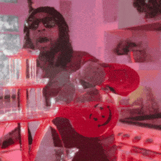 a man wearing sunglasses is pouring a drink from a red pitcher with a smiley face on it