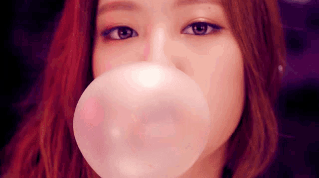 a close up of a woman blowing a pink bubble