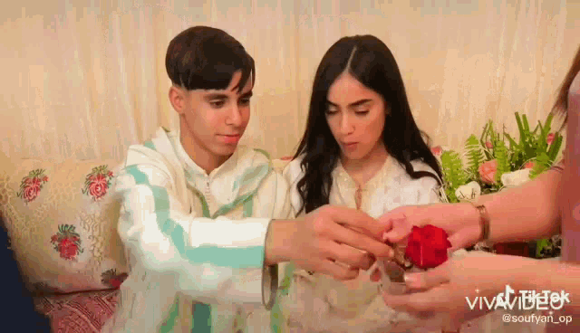 a man is putting a ring on a woman 's finger while a woman holds a rose .