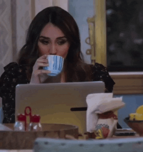 a woman is drinking a cup of coffee while using a tablet computer .
