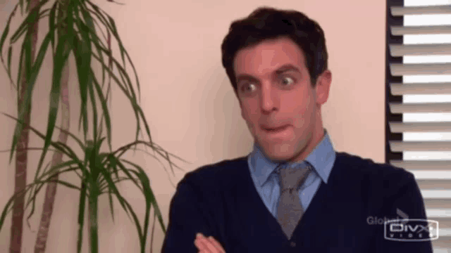 a man in a blue shirt and tie is making a funny face in front of a window .
