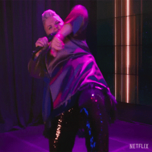 a woman is singing into a microphone while dancing on a stage with a netflix logo in the background
